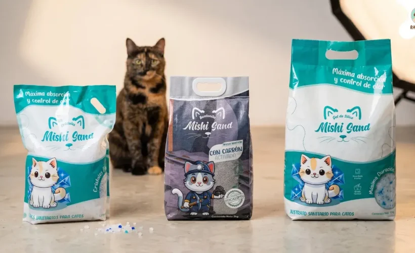 Tres empaques de arena para gatos Mishi Sand de 4kg, 5kg y 10kg en un estudio profesional con un gato sentado al fondo.